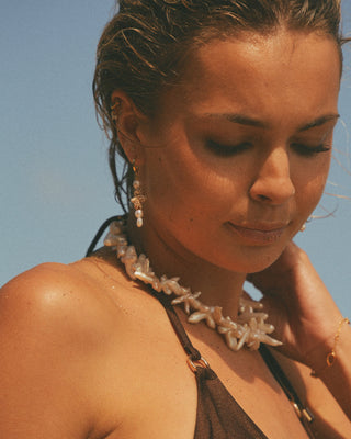 Model wearing a pearl necklace with a clear blue sky background