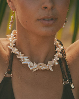 Close-up of a model wearing a cross pearl necklace and earrings with a blurred natural background