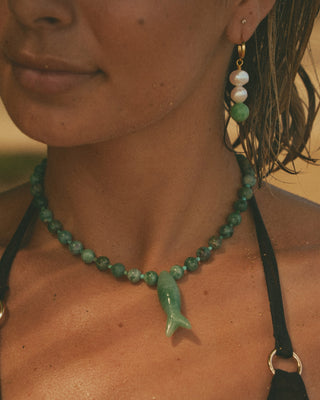 Close-up of a model wearing a green fish necklace and earrings with a blurred background