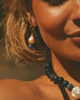 Close-up of a model wearing pearl earrings and a necklace with stone beads.