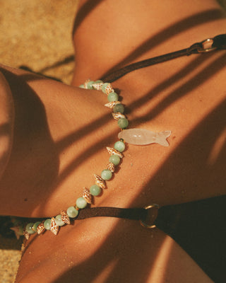Close-up of a necklace with moonstone beads and fish pendant on a model's neck.