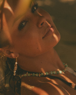 Close-up of a model wearing a beaded necklace and earring with a warm, golden light.