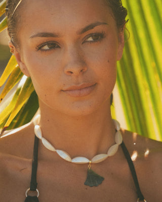 Model wearing a shell necklace with a tropical background