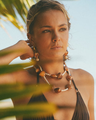 Model wearing a shell necklace with a tropical background