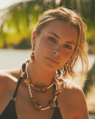 Model wearing a pearl and shell necklace with a blurred natural background