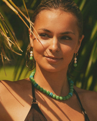 Model wearing a green beaded necklace and earrings with a blurred natural background
