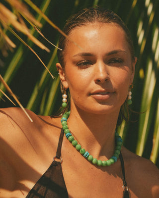 Model wearing a green beaded necklace with a tropical background