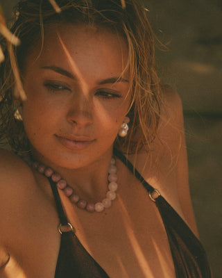 Model wearing a brown bikini and pearl necklace with a blurred natural background