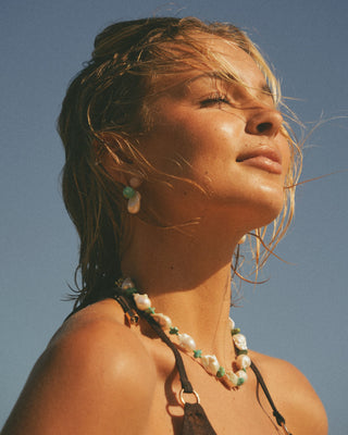 Model wearing a pearl necklace with wet hair against a clear blue sky