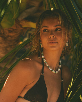 Model wearing a brown bikini and pearl necklace among tropical plants