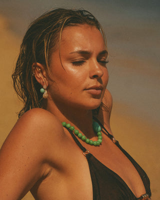Model wearing a green beaded necklace against a warm-toned background