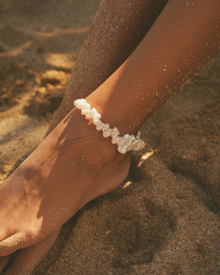 Close-up of a foot wearing a pearl anklet on a sandy background