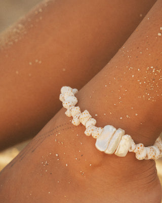 Beach-themed anklet on a model's wrist with sand particles.
