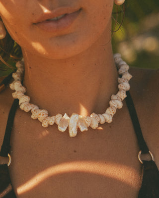 Model wearing a pearl and shell necklace with a blurred natural background