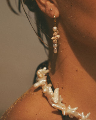 Close-up of a model wearing pearl earrings with a neutral background