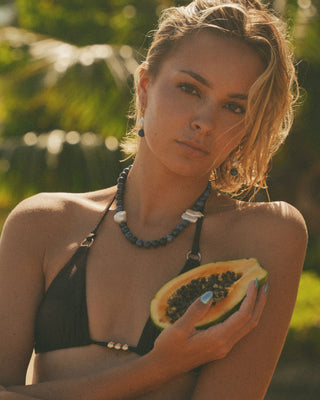 Model wearing a pearl jewelry holding a papaya in a tropical setting