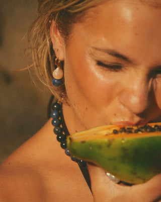 Woman wearing a jewelry eating a piece of fruit with a blurred background