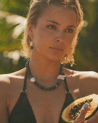Model holding a papaya wearing a necklace with a blurred green background